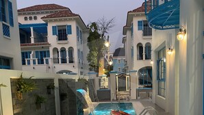 A swimming pool with a waterfall feature, surrounded by buildings with blue shutters and white walls. - Sun Grand Feria (Bai Chay)