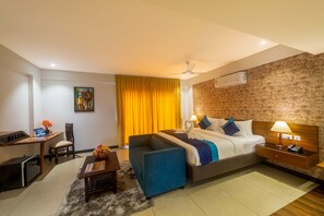 A hotel room with a bed, a desk, a chair, a sofa, and a small table with a lamp and a phone. - Royal Ace Boutique Hotel (Bengaluru)