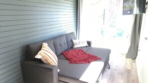 Un sofá de esquina con una manta roja y almohadas a rayas, frente a una pared azul.