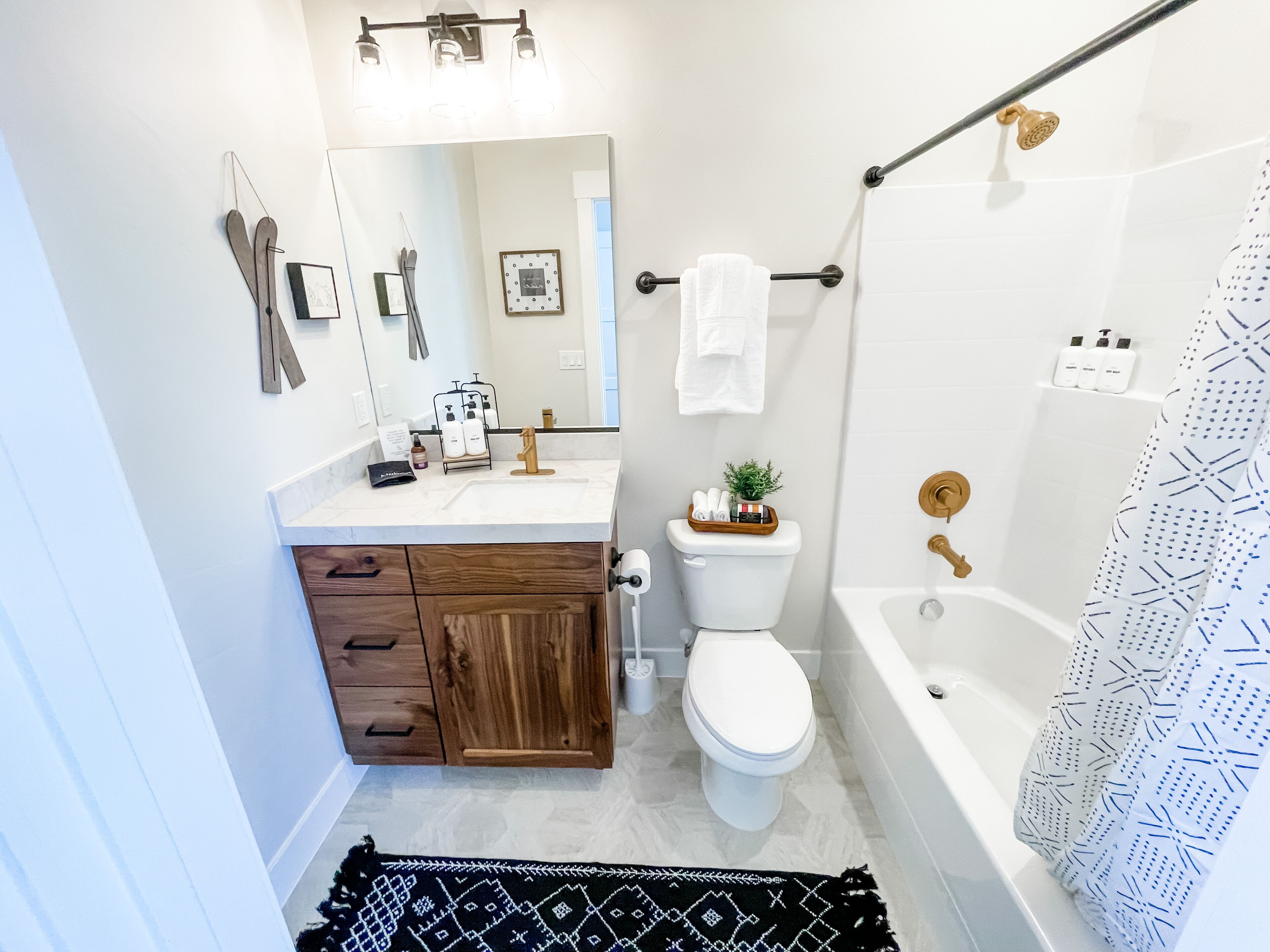 Un bagno con lavandino bianco, mobiletto in legno, un water, una vasca da bagno e una tenda da doccia.