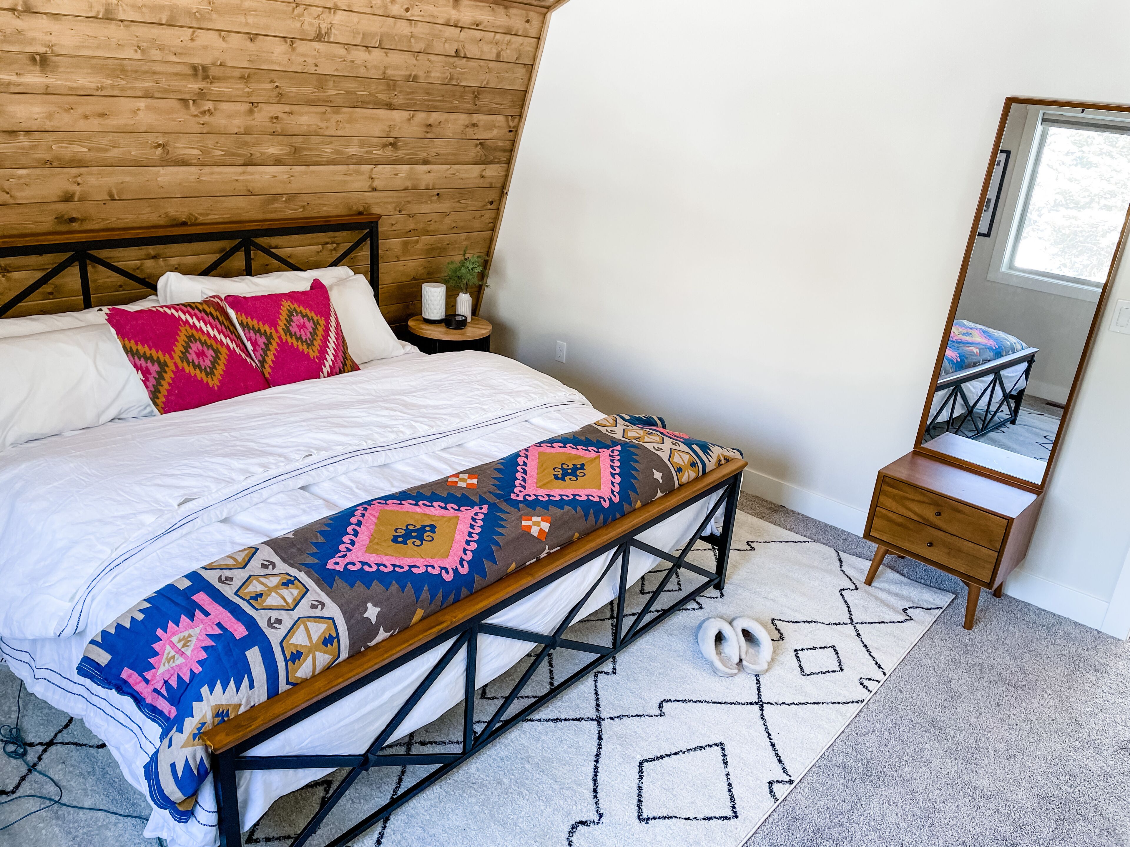 Een slaapkamer met een houten hoofdbord, een bed met behang, een nachtkastje met een vaas en een spiegel.