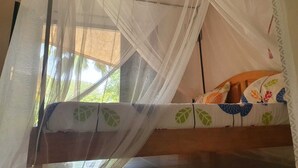 A room with a bed under a mosquito net, a window with a view of greenery, and a bed with a colorful floral bedspread. - Villa Sarrène (Nianing)