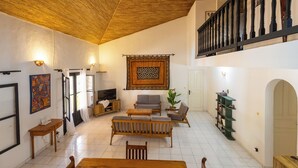 A spacious living area with a wooden ceiling, a sofa set, a television, and a bookshelf. - Villa Sarrène (Nianing)