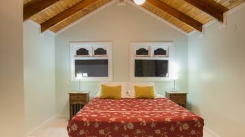 A bedroom with a sloped ceiling, two windows with shutters, a bed with a floral bedspread, and bedside lamps.