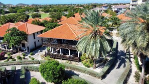 A multi-story building with a red-tiled roof, surrounded by palm trees and a landscaped garden. - VIP Blue Bay Beach Villa 33 (Sint Michiel)