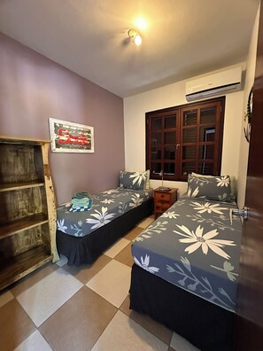 A bedroom with two single beds, a wooden wardrobe, a window with a view, and a wall-mounted air conditioner. - VIP Blue Bay Beach Villa 33 (Sint Michiel)