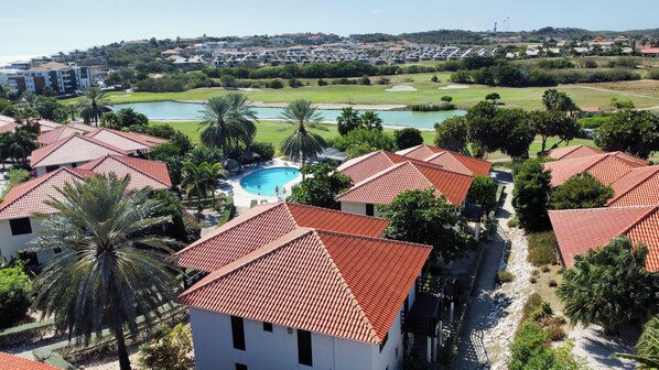 A resort with red-tiled roofs, a swimming pool, and a golf course in the background. - VIP Blue Bay Beach Villa 33 (Sint Michiel)