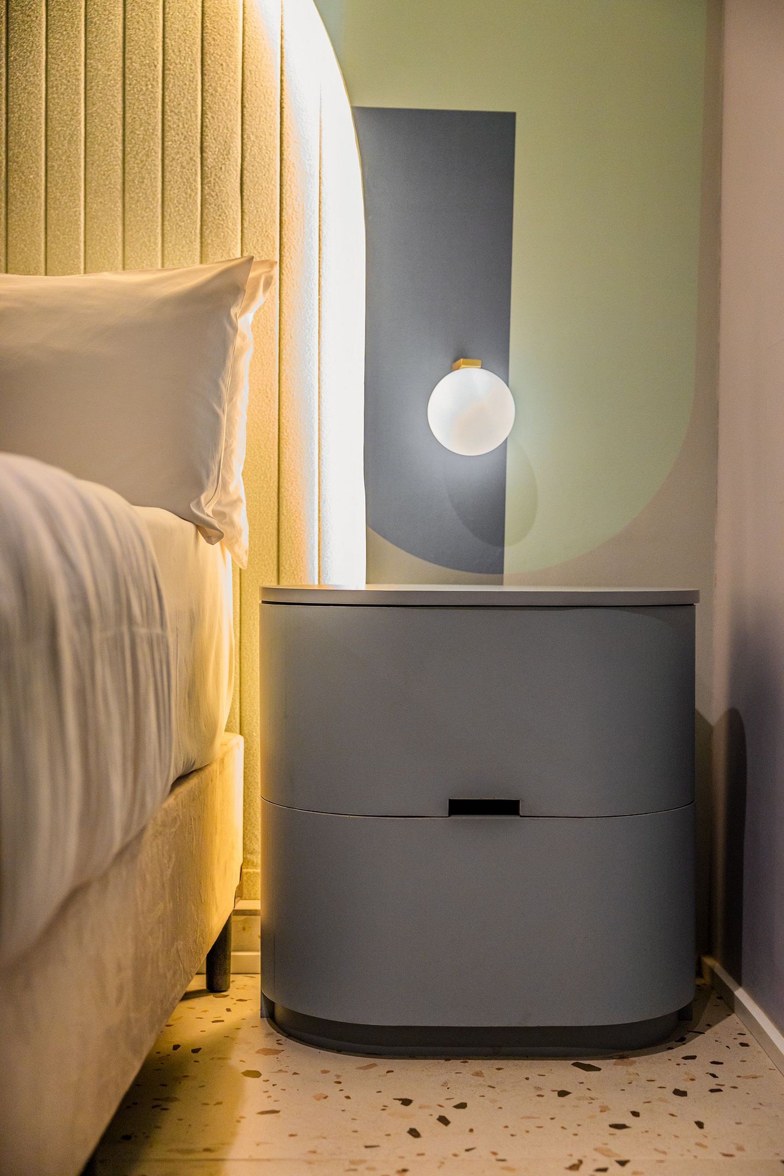 Een moderne slaapkamer met een bed, nachtkastje en een wandlamp.
