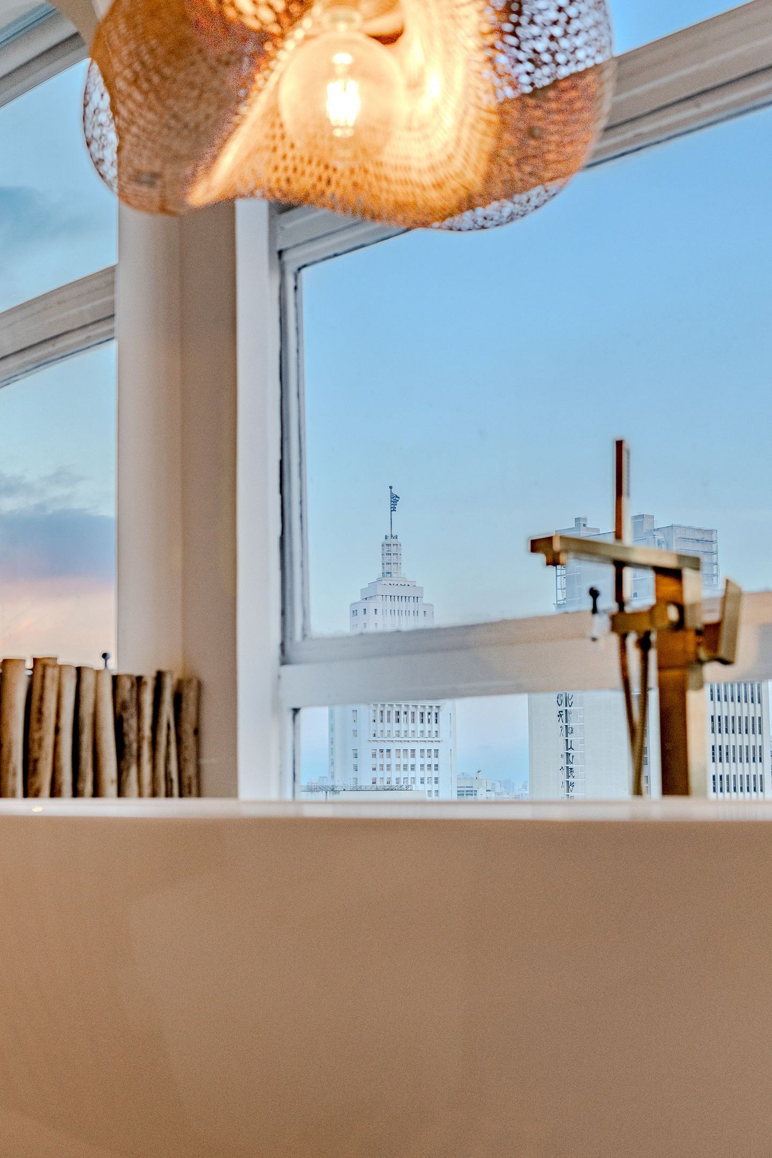 A room with a large window, a hanging light fixture, and a wooden structure on the windowsill.