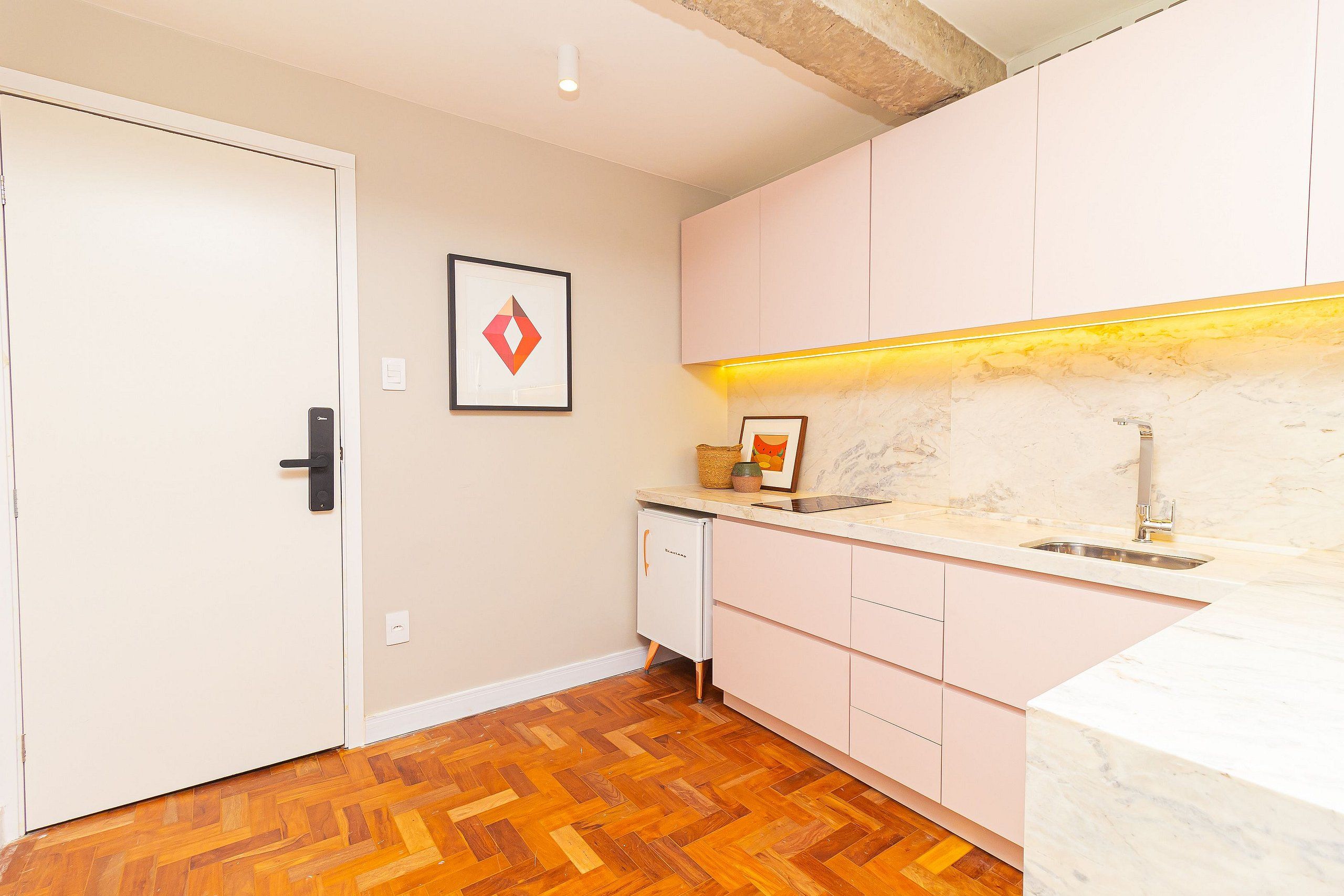 A kitchen with a wooden herringbone floor, white cabinets, a marble countertop, and a built-in dishwasher.