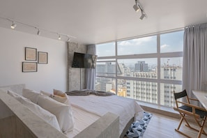 A modern bedroom with a large bed, a TV mounted on the wall, and a city view through large windows. - Vossa Bossa Sky Mirante (São Paulo)