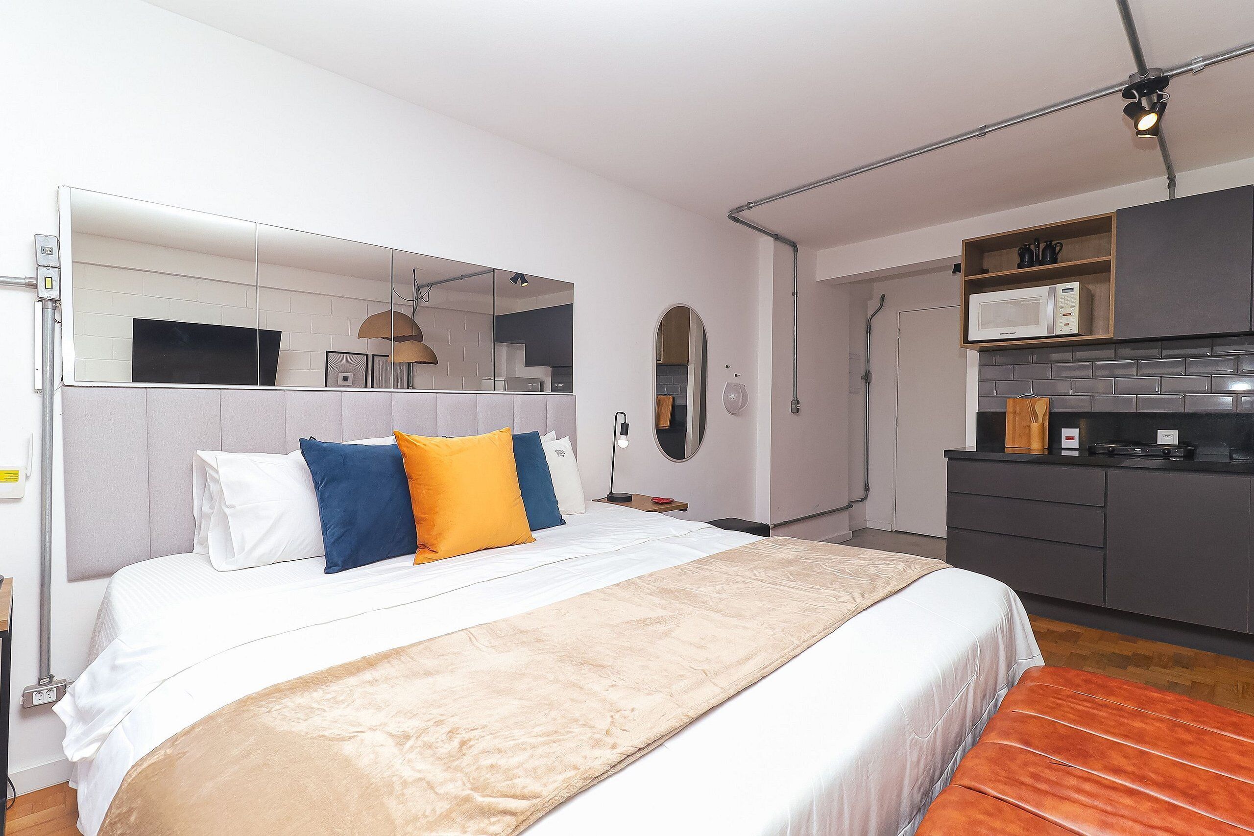 Quarto de hotel moderno com cama grande, TV embutida, micro-ondas e cozinha compacta.
