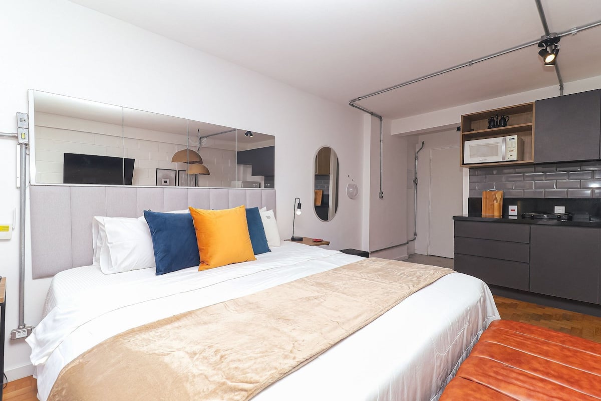 Una habitación de hotel moderna con una cama grande, una zona de cocina con microondas y un espejo sobre la cama.