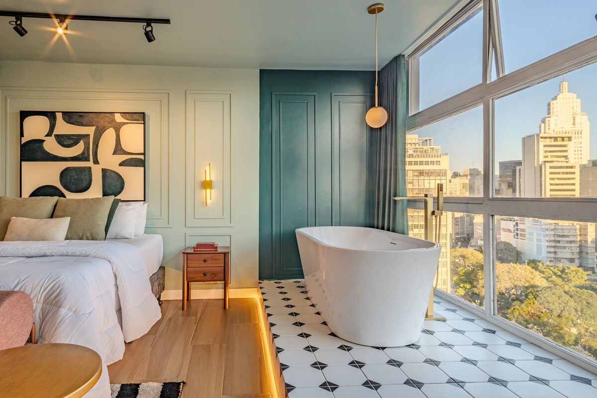 A bedroom with a large window, a bathtub, and a city view.