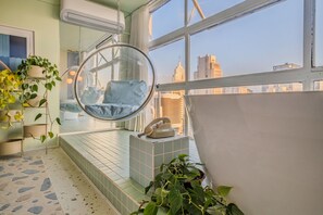 A room with a hanging chair, a telephone, and a view of the cityscape through large windows.