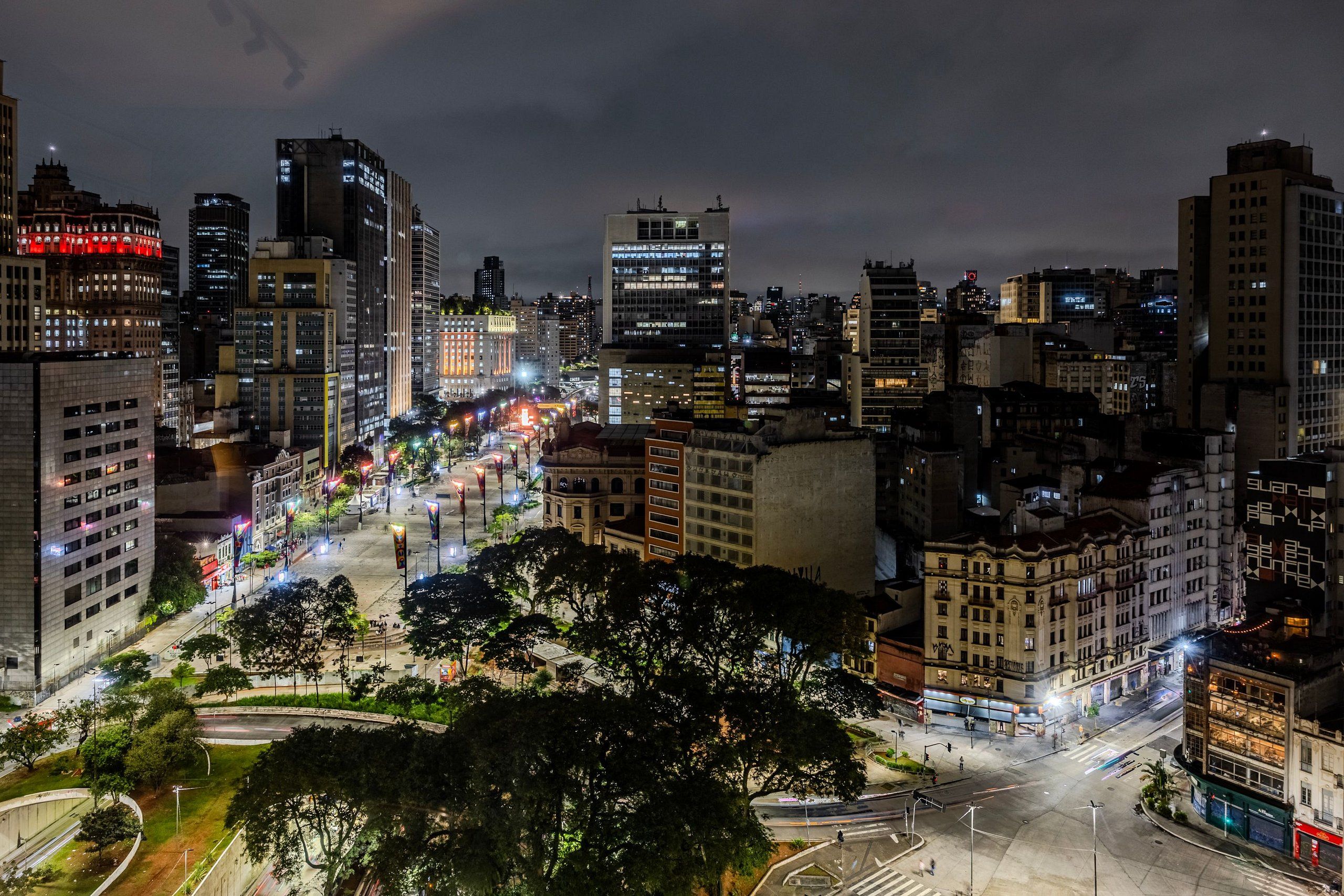 Un paisaje urbano nocturno con edificios iluminados y una glorieta central.