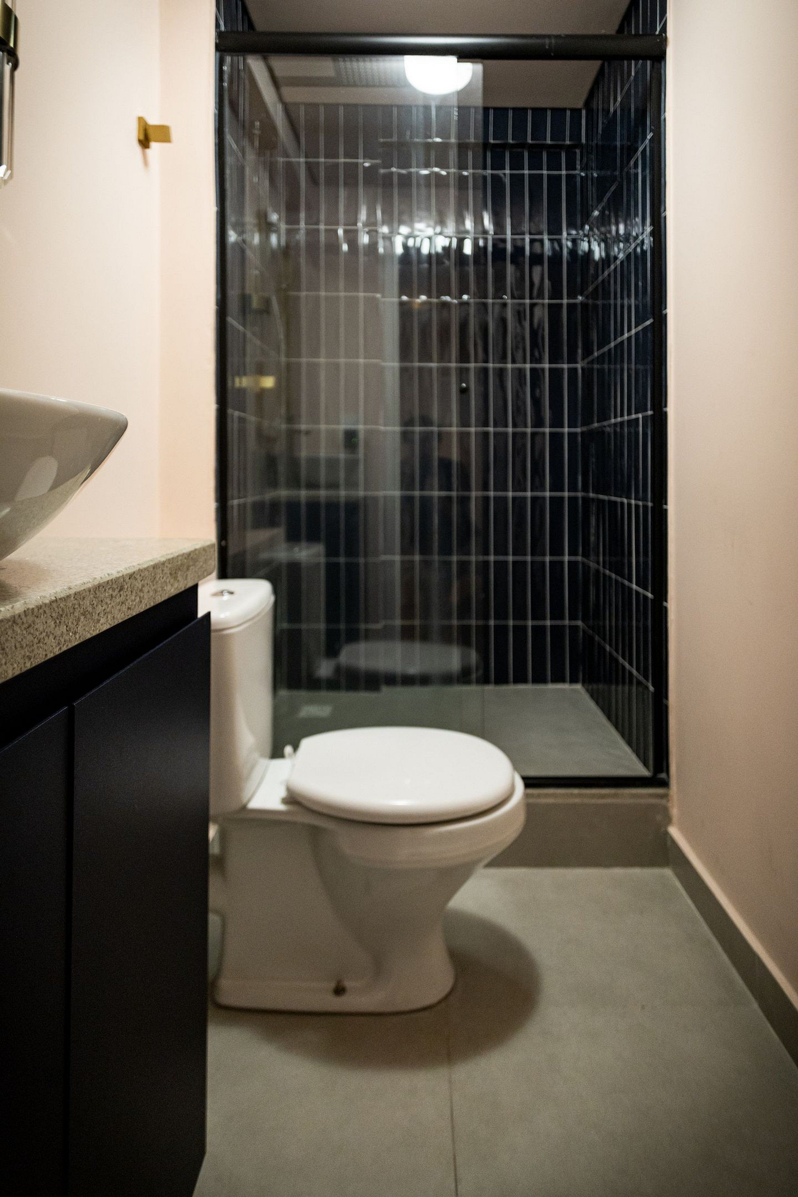 A small, enclosed bathroom with a toilet, a sink, and a shower area.