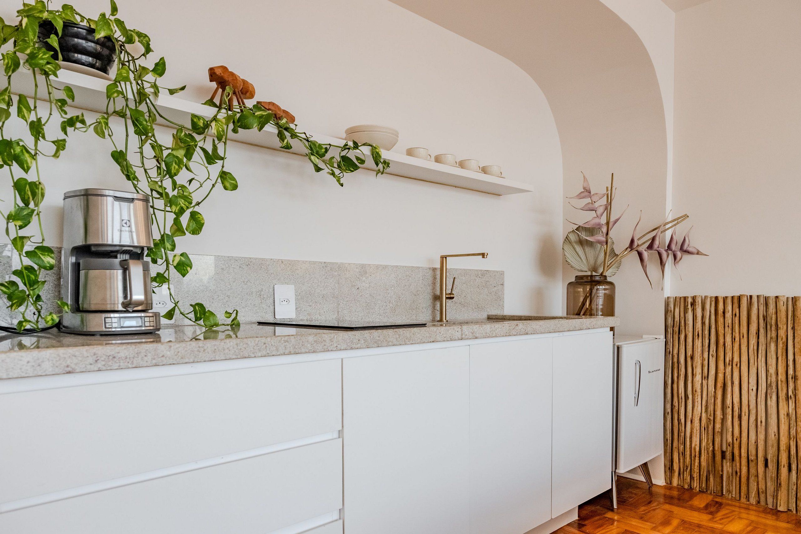 A modern kitchen with white cabinets, a stainless steel coffee maker, a sink, and a wooden wall panel.