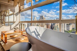 A modern bathroom with a freestanding bathtub, a round mirror, and a view of a cityscape through large windows. - Vossa Bossa Sky Mirante (São Paulo)