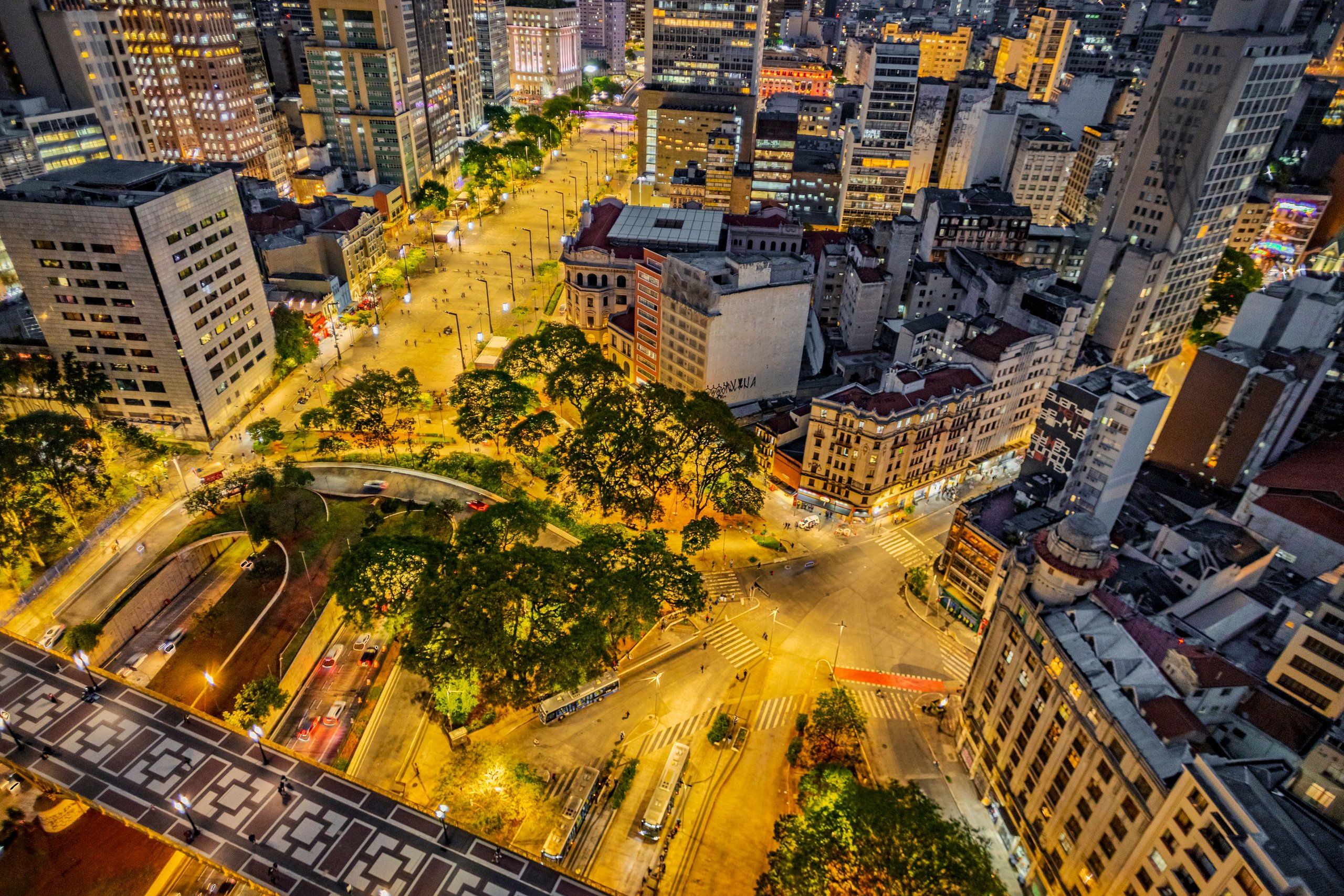 An aerial view of a cityscape at night with illuminated buildings, roads, and a bridge.