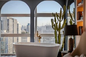 A room with a bathtub, a cactus plant, and a view of a cityscape through arched windows.