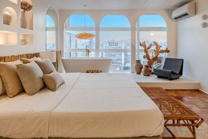 Um quarto espaçoso com uma cama grande, uma banheira e vista para a cidade através de janelas em arco.