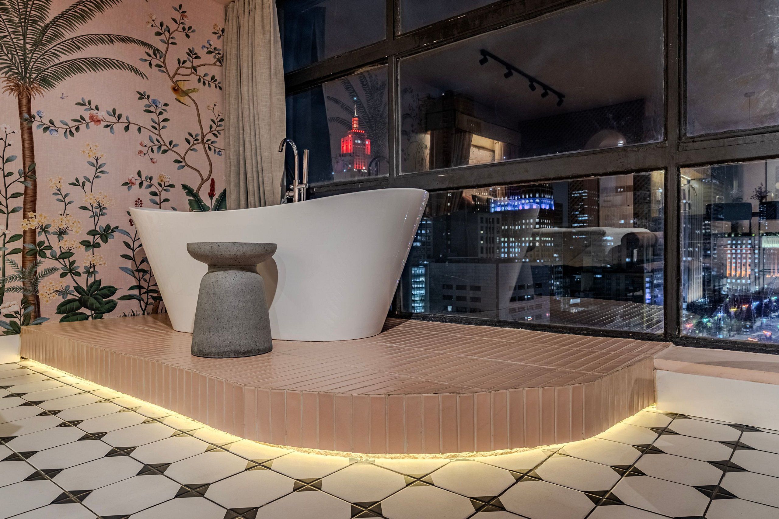 Un bagno moderno con una vasca freestanding, un elemento decorativo in pietra e vista sulla città di notte.