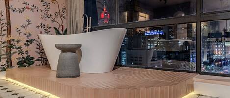 Un bagno moderno con una vasca freestanding, un elemento decorativo in pietra e vista sulla città di notte.
