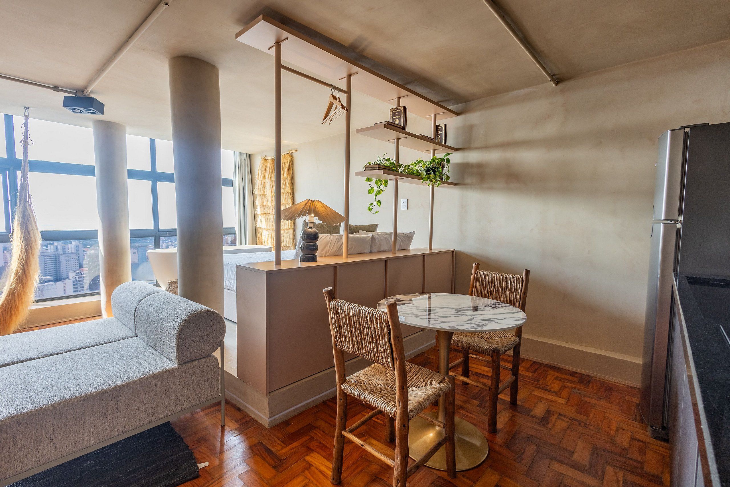 A modern living space with a sofa, dining table, chairs, a kitchen area, and a view of the city.