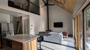 Eine moderne Küche mit einer großen Kochinsel, einem Essbereich mit einer Couch und Stühlen, einem an der Wand montierten Fernseher und einem großen Fenster mit Blick ins Freie.