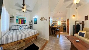 A bedroom with a bed, a wooden floor, a kitchen area with a dining table, and a living room with a sofa.