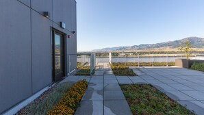 Un edificio moderno con puerta de vidrio, un camino que lleva a una cerca metálica y vista de montañas al fondo.