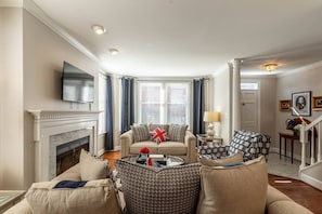 A living room with a fireplace, a sofa set, a television mounted on the wall, and a staircase leading to another level.