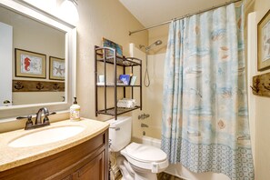 Ein Badezimmer mit Waschbecken, Toilette und Dusche. Über der Toilette befindet sich ein Regal mit Büchern und einer Flasche.