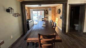 A wooden dining area with a long table and benches, a kitchen visible through an open door, and a rustic interior design.