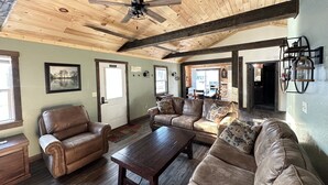 A spacious living room with a high wooden ceiling, leather sofas, a wooden coffee table, and a ceiling fan.