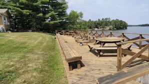 A wooden deck with picnic tables and benches by a lake.