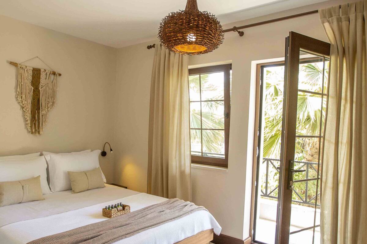 Un dormitorio con una cama grande, una lámpara colgante y vistas a través de una puerta abierta.
