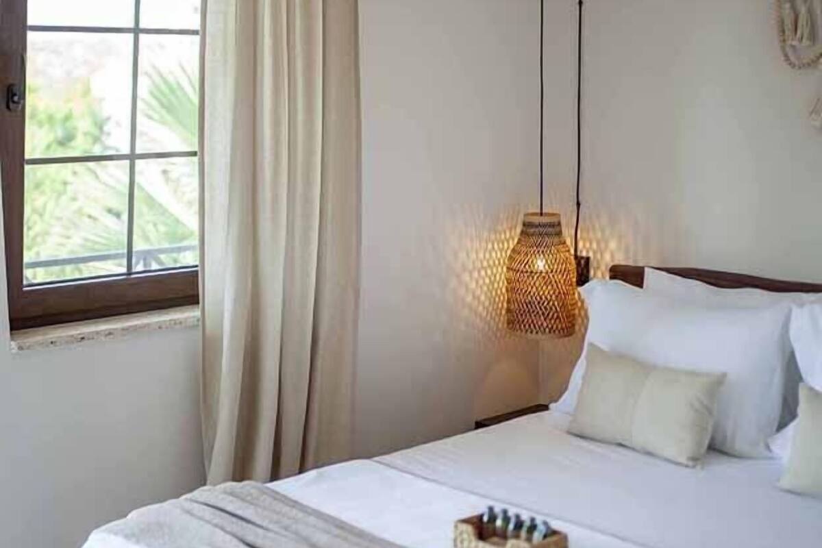 Un dormitorio con cama, ventana con cortinas y dos lámparas colgantes.