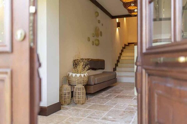 A hallway with a wooden door, a stone-tiled floor, a sofa, wicker baskets, and a staircase. - Finka Hotel (Bozcaada)