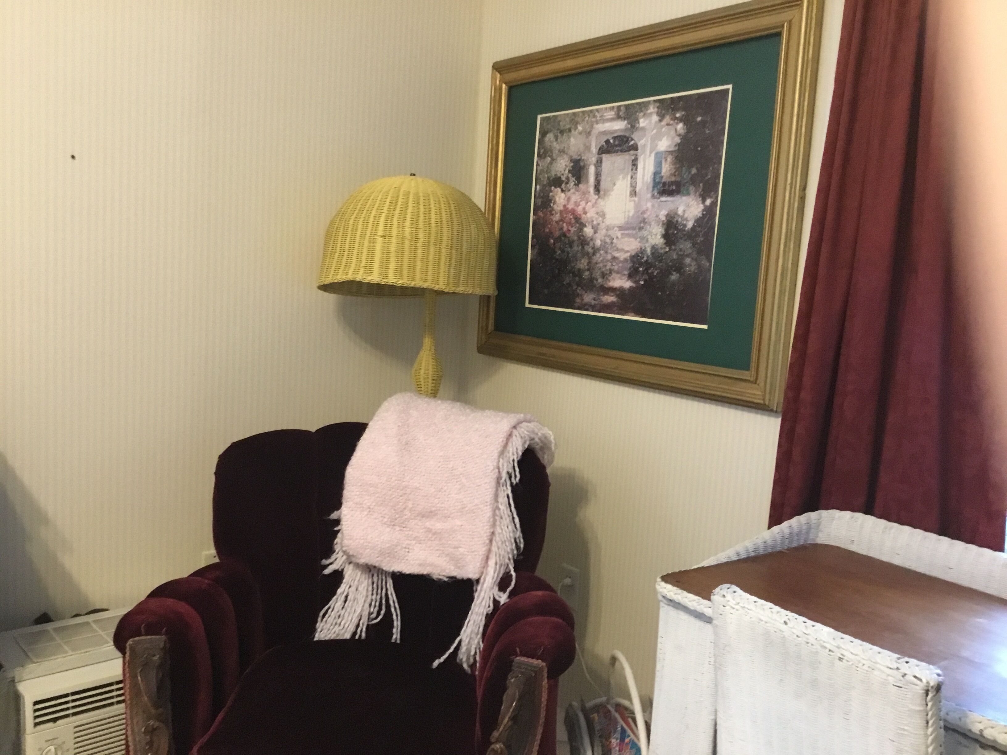 A room with a dark red armchair, a white chair, a yellow lamp, and a framed picture on the wall.
