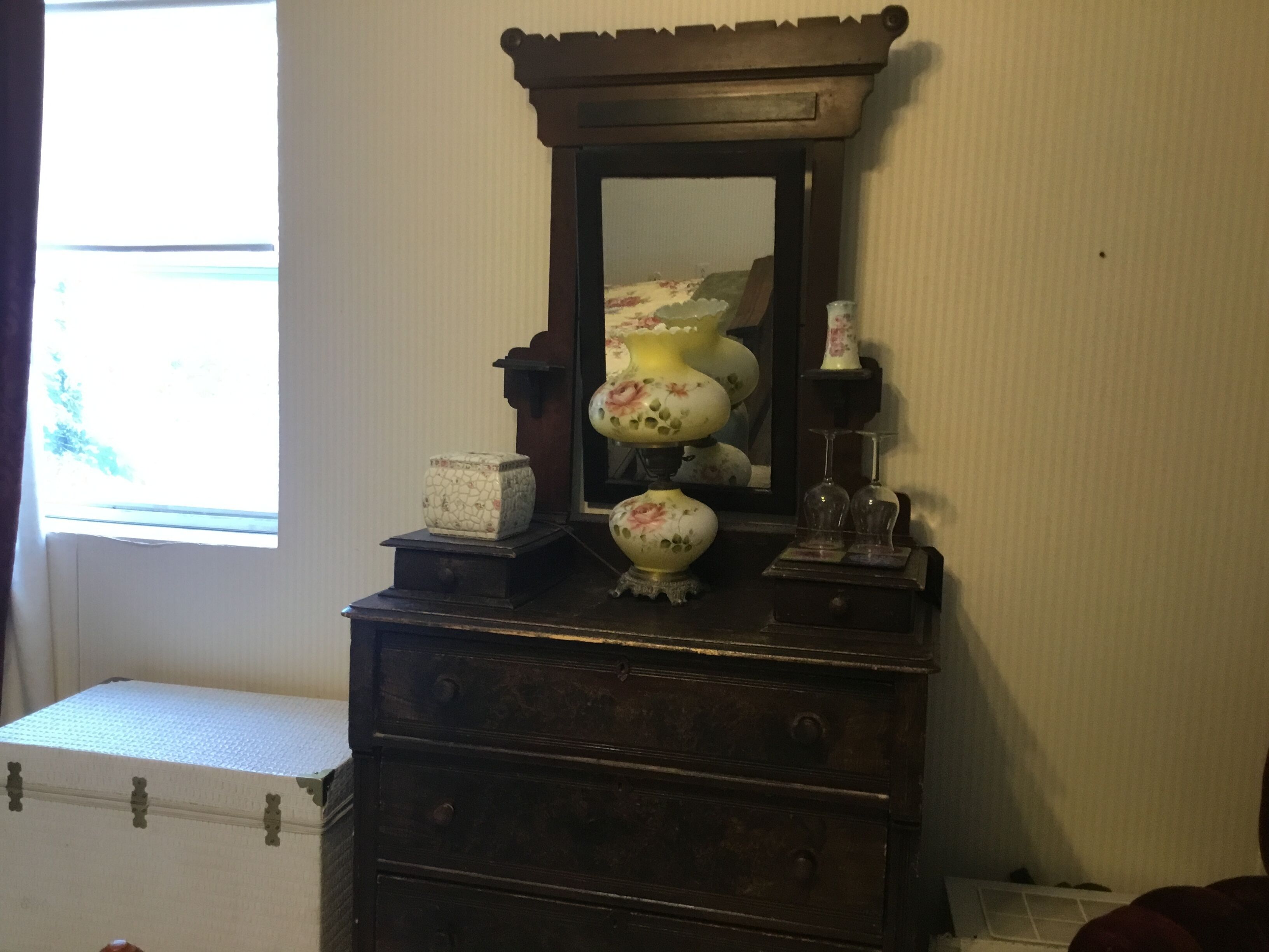 A wooden dresser with a mirror, a vase, and a small clock.