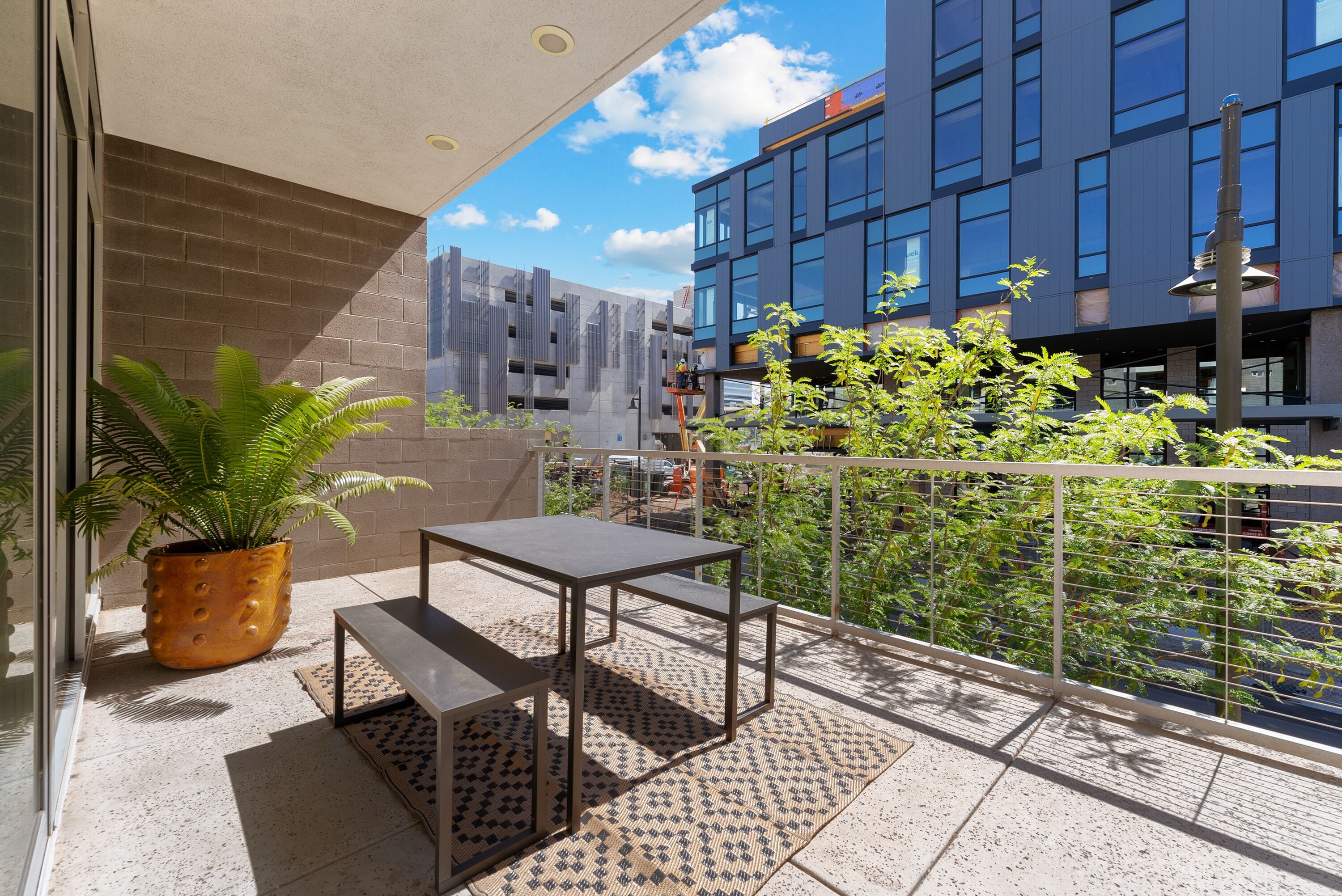 A balcony with a potted plant, a metal table, and a patterned rug.
