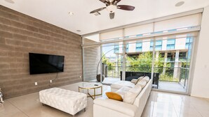 A modern living room with a sofa, ottoman, and a flat-screen TV mounted on a brick wall. - Tempe Lofts (Tempe)
