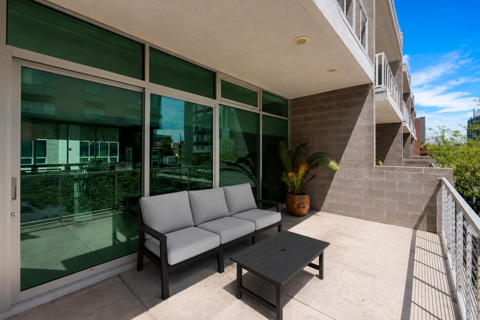 A balcony with a grey sofa, a small table, and a potted plant.