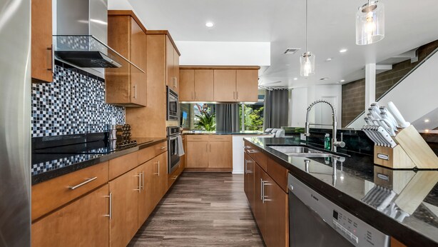 A modern kitchen with wooden cabinets, a black and white checkered backsplash, stainless steel appliances, and pendant lighting. - Tempe Lofts (Tempe)
