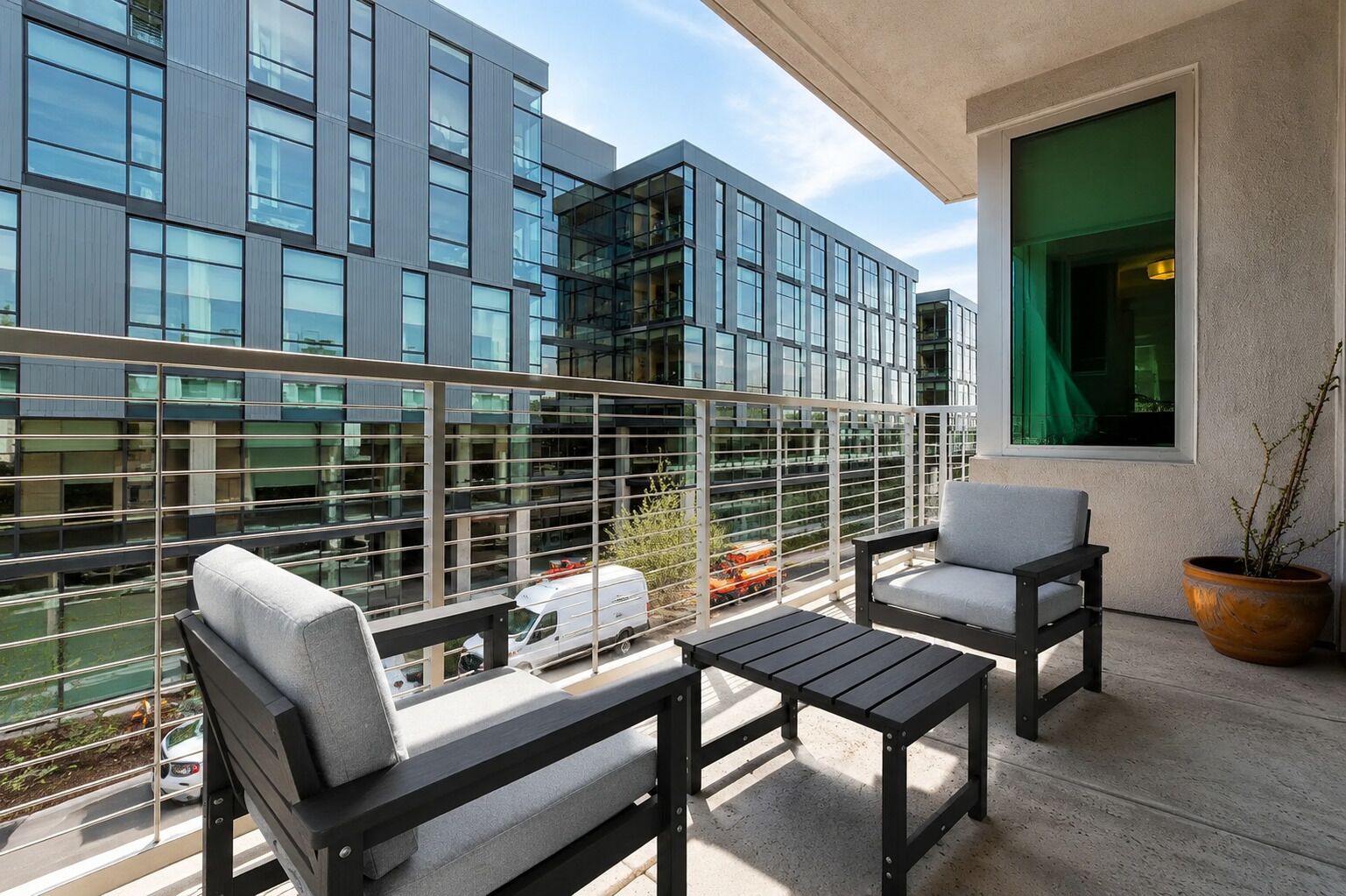 A balcony with two chairs and a table, overlooking a modern building with large windows.