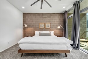 A modern bedroom with a large bed, two bedside lamps, and a brick accent wall. - Tempe Lofts (Tempe)