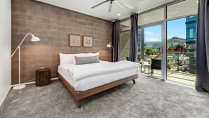 A modern bedroom with a large bed, a ceiling fan, and a view of the city through large windows. - Tempe Lofts (Tempe)