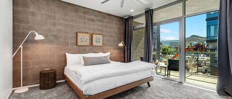 A modern bedroom with a large bed, a ceiling fan, and a view of the city through large windows.